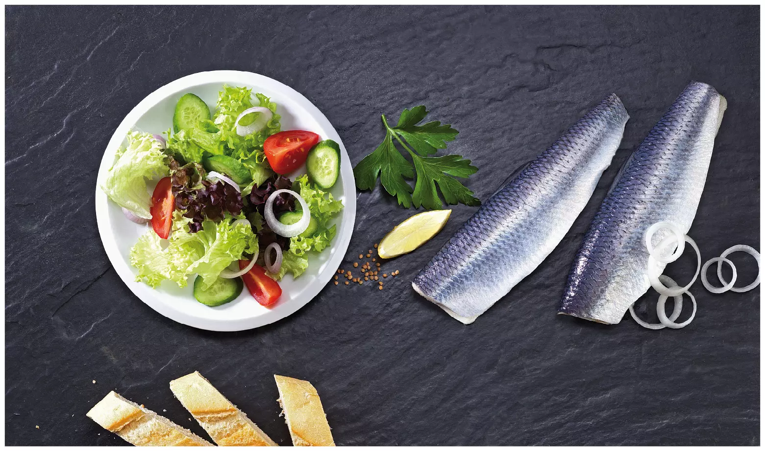zwei Matjesfilets mit Haut neben Salat, Zwiebeln und Brot