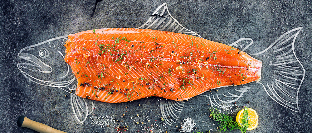 Ein großes, rohes Lachsfilet mit Kräutern und Gewürzen auf einer Tafel, dekoriert mit Zeichnungen eines Fisches, einer Zitrone und Dill.