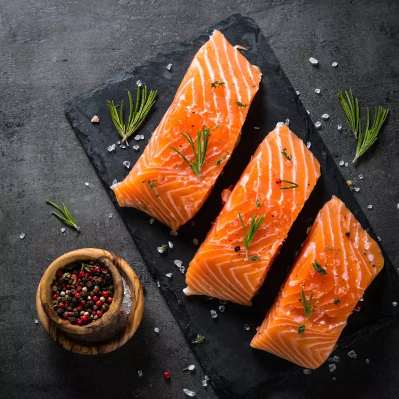 drei rohe Lachsfilets auf Schieferplatte mit Kräutern