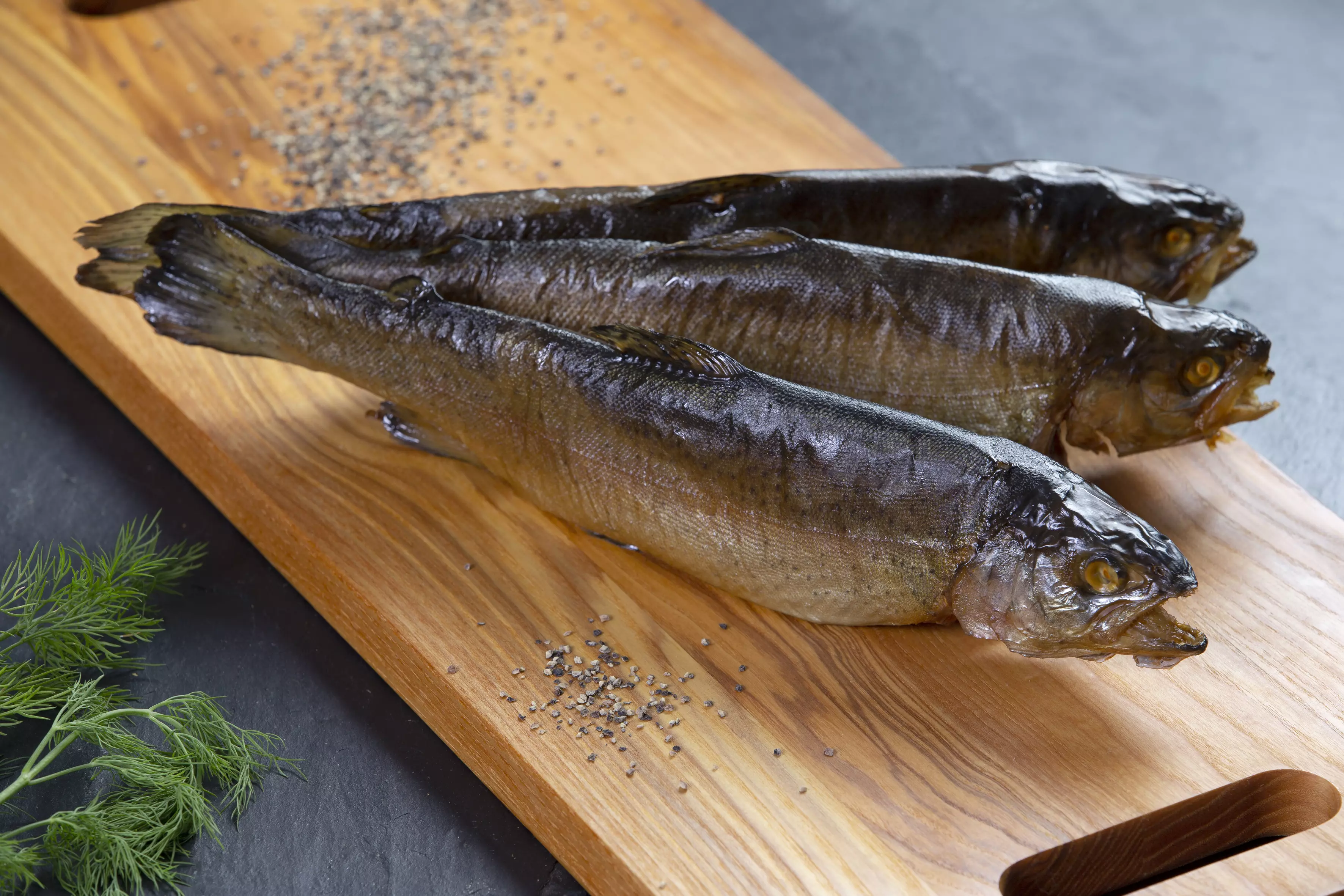 drei ganze Räucherforellen auf Holzbrett serviert