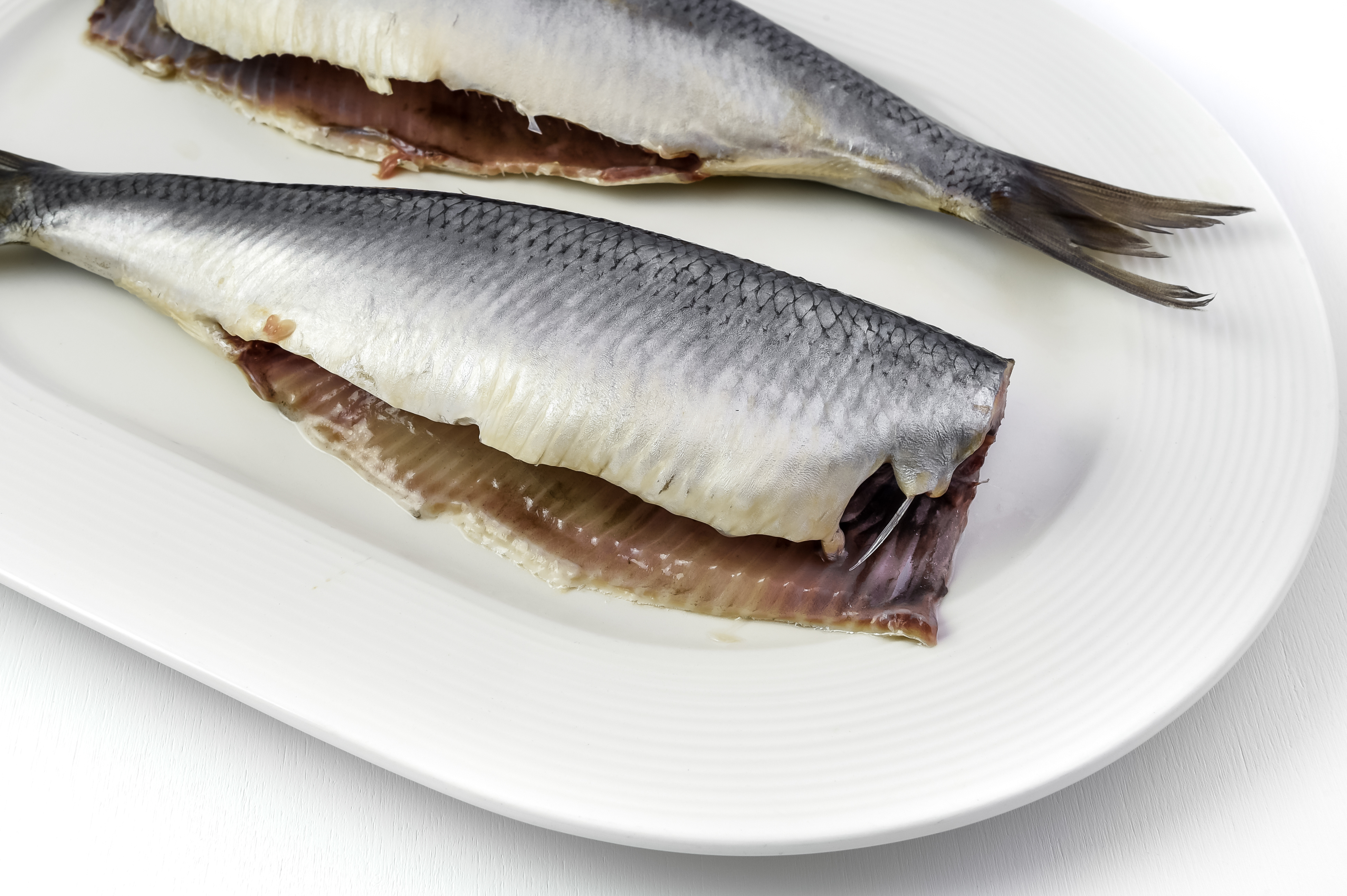 zwei rohe Matjesheringe mit Haut auf weißem Teller