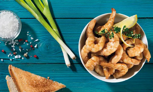 Schale mit Garnelen, Zitrone und Kräutern auf blauem Tisch