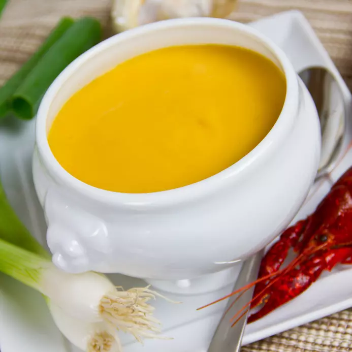 gelbe Krabbencremesuppe in weißer Schale mit Lauch und Garne