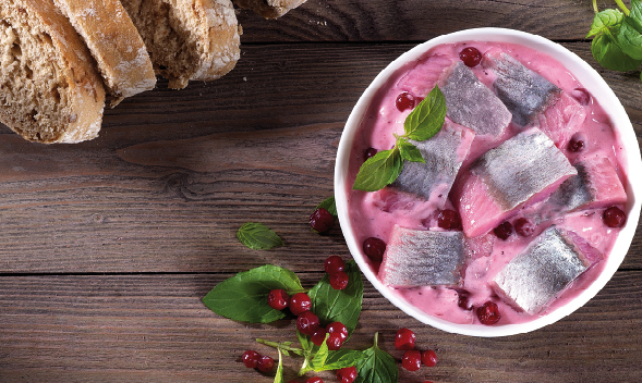 Heringssalat mit Preiselbeeren und Brot auf Holztisch Ein Schüssel Heringssalat mit Preiselbeeren und frischen Kräutern, daneben liegt rustikales Brot auf einem Holztisch.