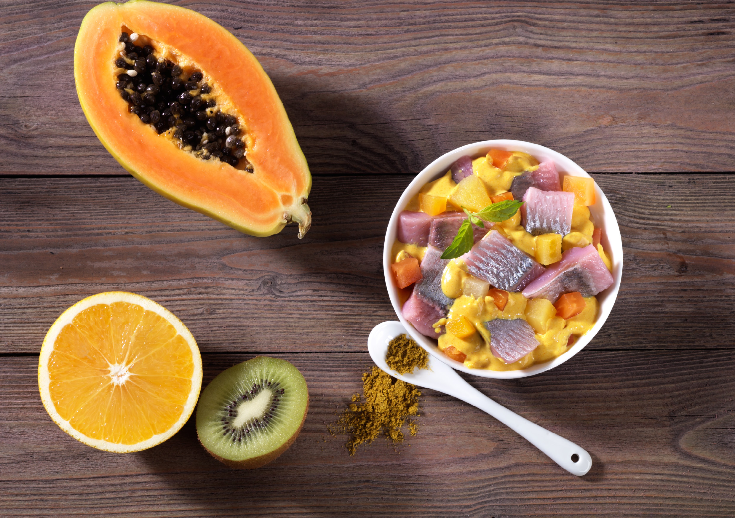 Geschnittene Papaya, Orange, Kiwi und ein exotischer Teller mit Fisch und Currypulver auf einem Holzuntergrund