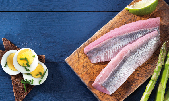 Frische Heringfilets mit Brot, Ei und Spargel Zwei Heringfilets auf einem Schneidebrett mit einer Limettenscheibe, daneben Roggenbrot mit gekochten Eierscheiben und Spargel auf blauem Hintergrund