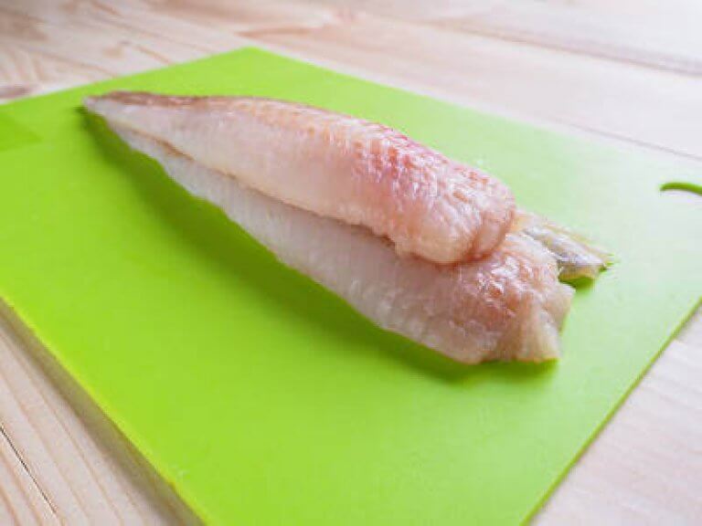 Frisches Fischfilet auf grünem Schneidebrett Nahaufnahme eines rohen Fischfilets auf einem grünen Schneidebrett