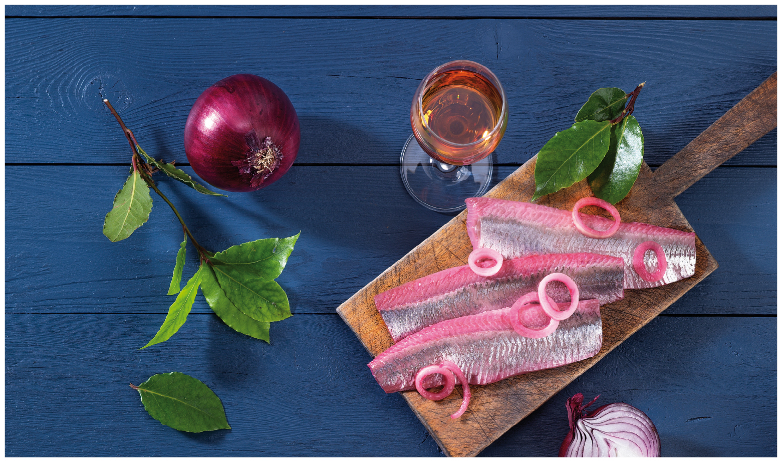 Heringsfilets mit Zwiebeln und Kräutern auf Holzbrett Heringsfilets dekoriert mit roten Zwiebelringen und Kräutern auf einem Holzbrett, daneben Rotwein in einem Glas.