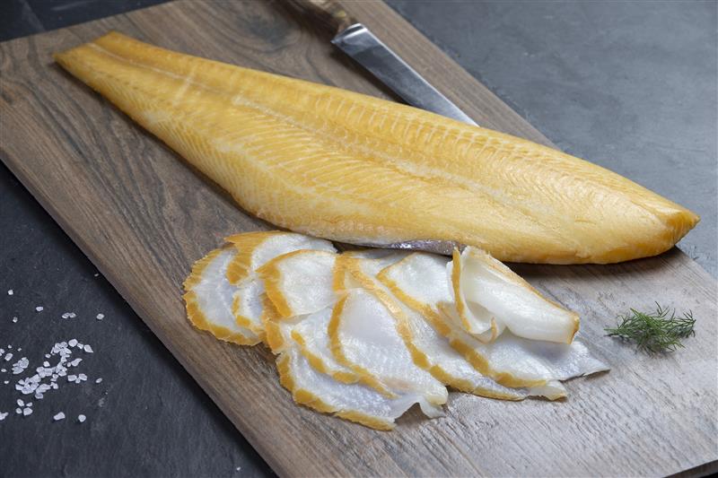 Geräucherter Fisch auf Schneidebrett mit Dill und Salz Ein großes Stück geräucherter Fisch liegt auf einem Holzschneidebrett, daneben sind dünne Scheiben des Fisches und ein Zweig Dill.