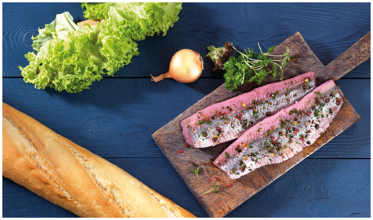 Frisches Heringsfilet mit Kräutern und Baguette Heringsfilet auf Holzbrett, garniert mit Kräutern und Gewürzen, daneben Baguette, Salat und Zwiebel auf blauem Untergrund