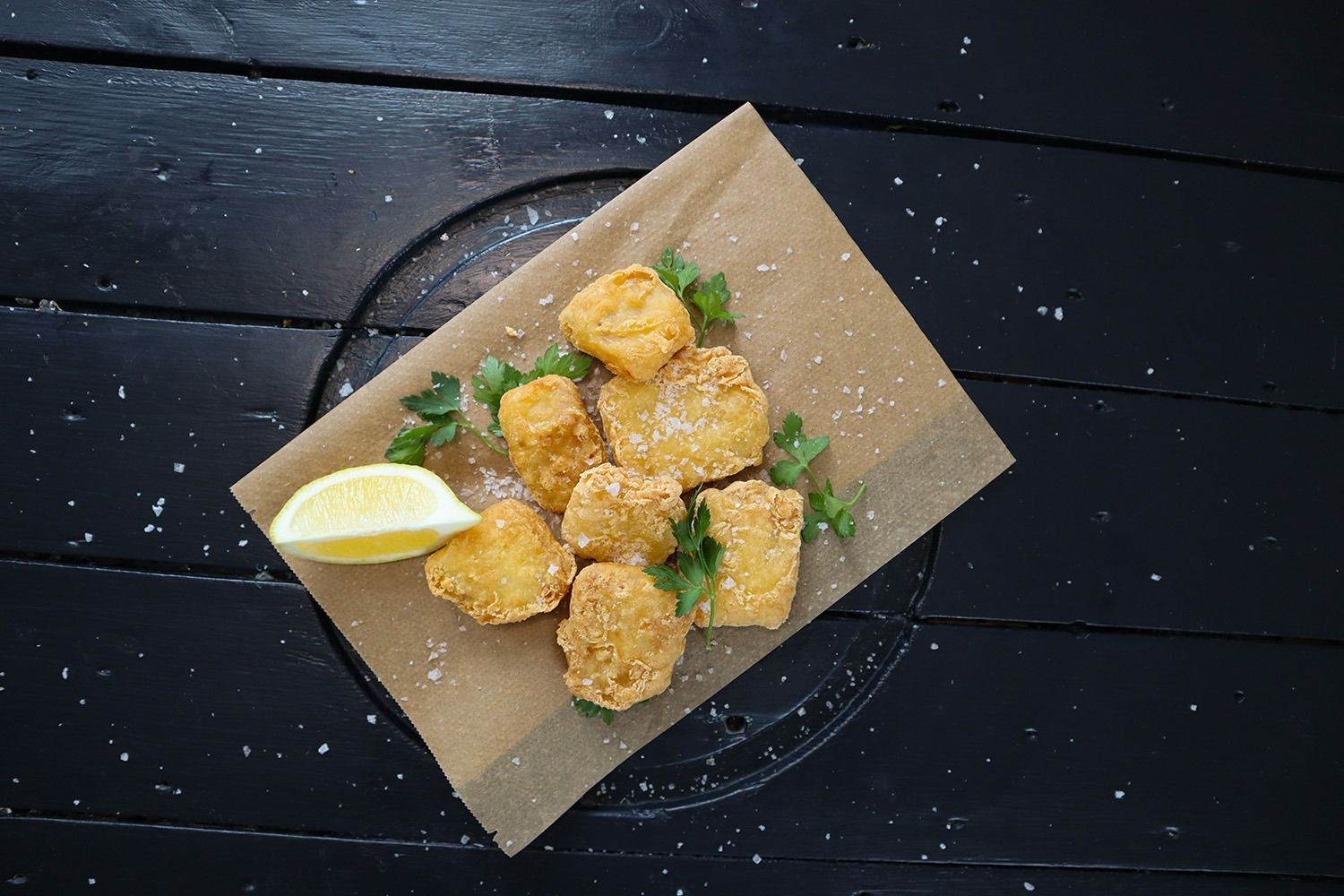 Frittierte Tofuwürfel serviert auf Packpapier mit Zitronenscheibe und Petersilie, dekoriert mit Meersalz