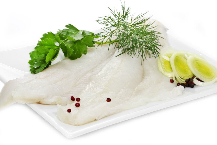 Frisches Fischfilet auf Teller mit Kräutern und Gemüse Weißes Fischfilet auf einem weißen Teller, garniert mit Petersilie, Dill, Lauch und roten Pfefferkörnern.