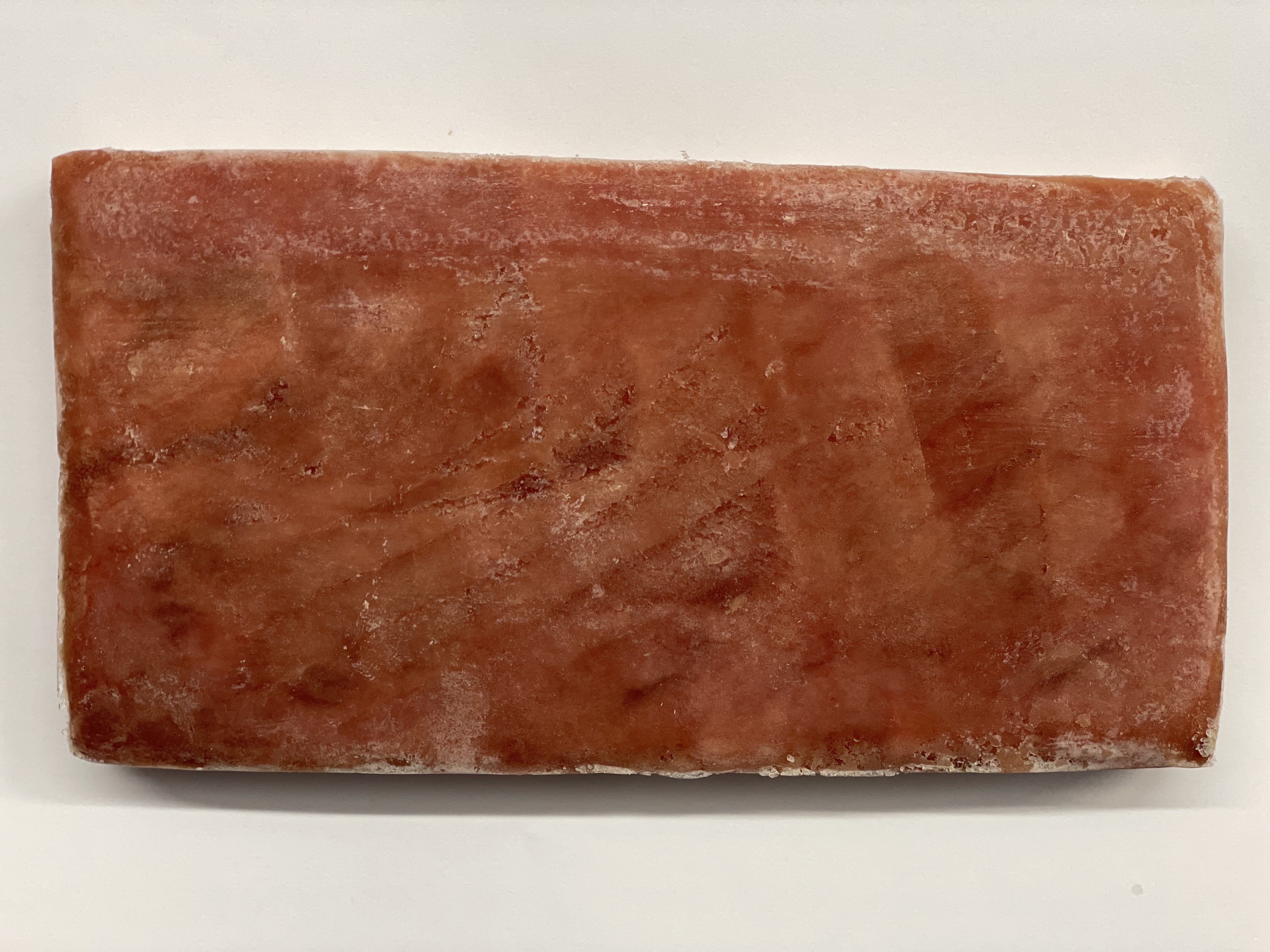 Ein gefrorenes Stück Lachsfilet liegt auf einer weißen Oberfläche. Das Filet hat eine rechteckige Form und ist leicht mit Frost überzogen.